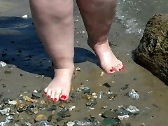 Fat naked legs with red pedicure walk along the bank of the river, fetish.